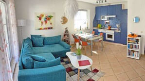Un salon avec un canapé, une table à manger avec des chaises, un coin cuisine avec des placards et un four à micro-ondes, et une bibliothèque.