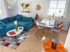Uma sala de estar com um sofá azul-turquesa, uma mesa de centro branca e uma área de jantar com mesa e cadeiras.