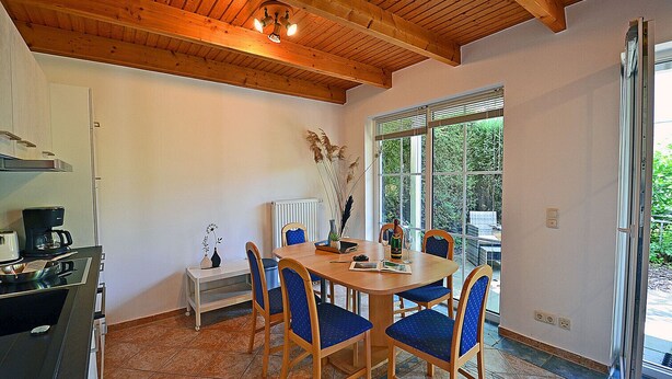 Un comedor con una mesa y sillas de madera, una cafetera y vistas a zonas verdes a través de grandes ventanales.