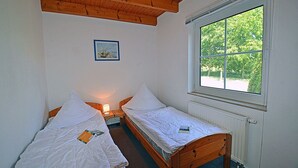 Una habitación con dos camas individuales, techo de madera, ventana con vista a follaje y un cuadro en la pared.