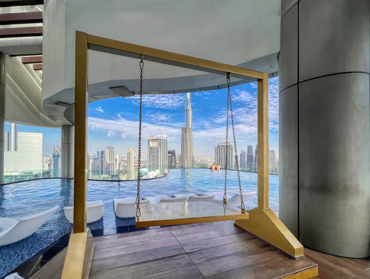 Une piscine intérieure luxueuse à débordement, dotée d’un fauteuil suspendu, et offrant une vue sur le panorama urbain.
