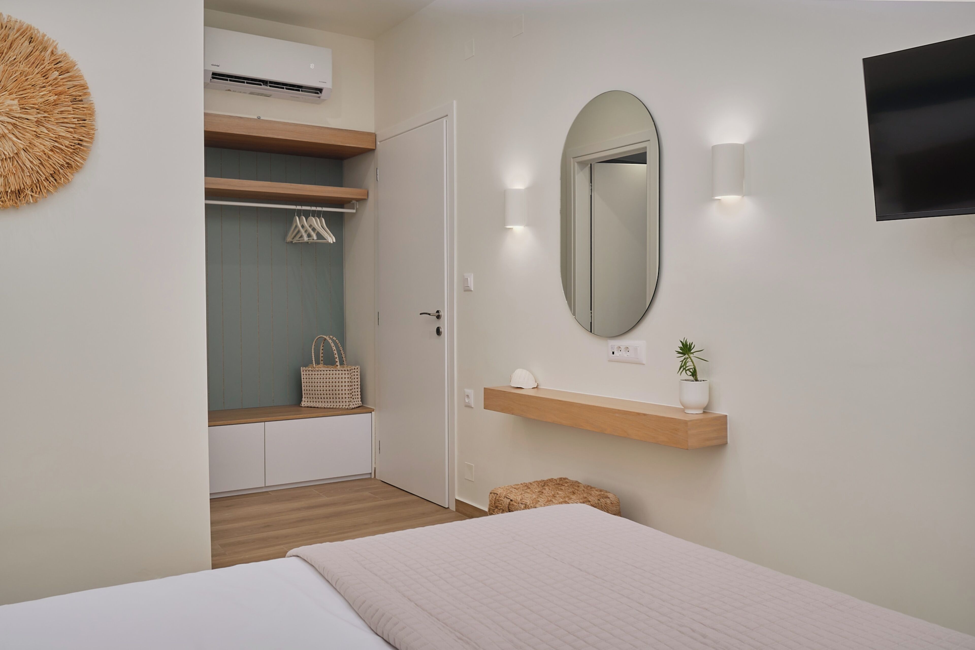 Une chambre à coucher comprenant un lit, une armoire, un miroir, une étagère avec une plante et un téléviseur fixé au mur.