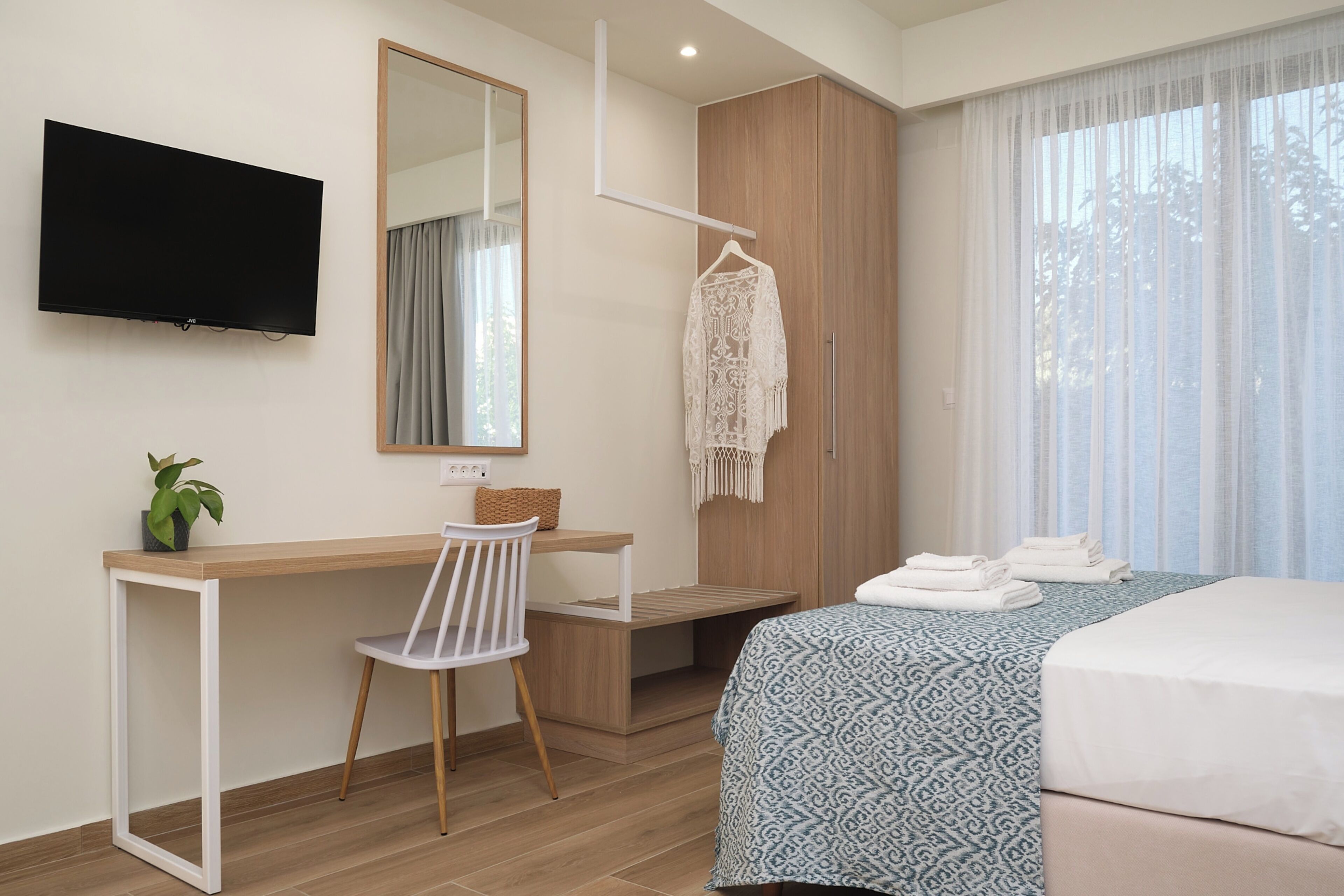 Ein Hotelzimmer mit Bett, Schreibtisch, Stuhl, Fernseher, Kleiderschrank und einem Fenster mit Vorhängen.