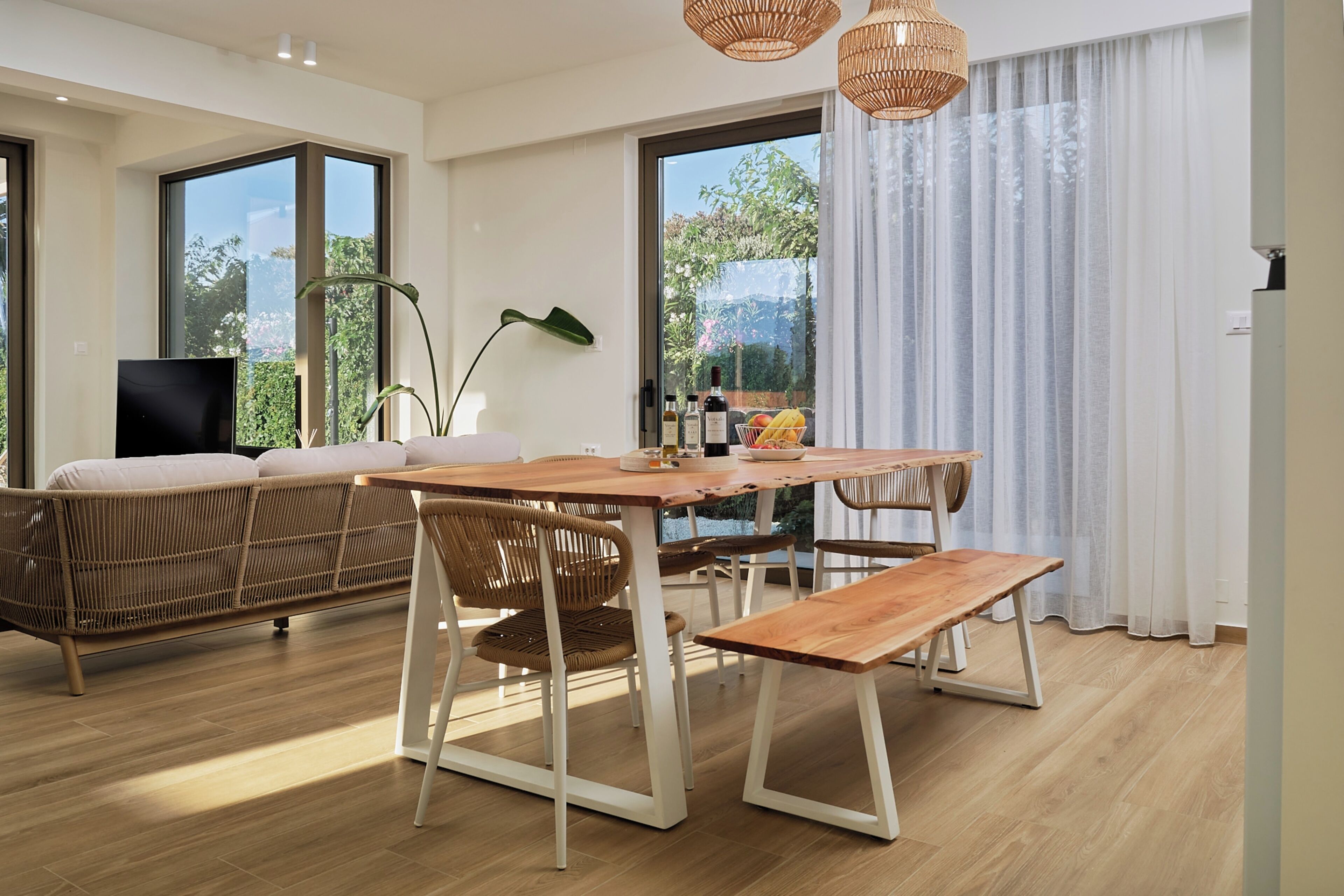 Un soggiorno moderno con un tavolo da pranzo in legno, mobili in vimini e ampie finestre con vista sul verde.