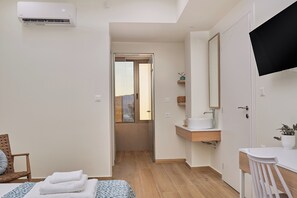 A modern bedroom with a bed, a bedside table, a TV, a bathroom with a sink and mirror, and a window. - Votsalo Seaside Villa (Kamisiana)