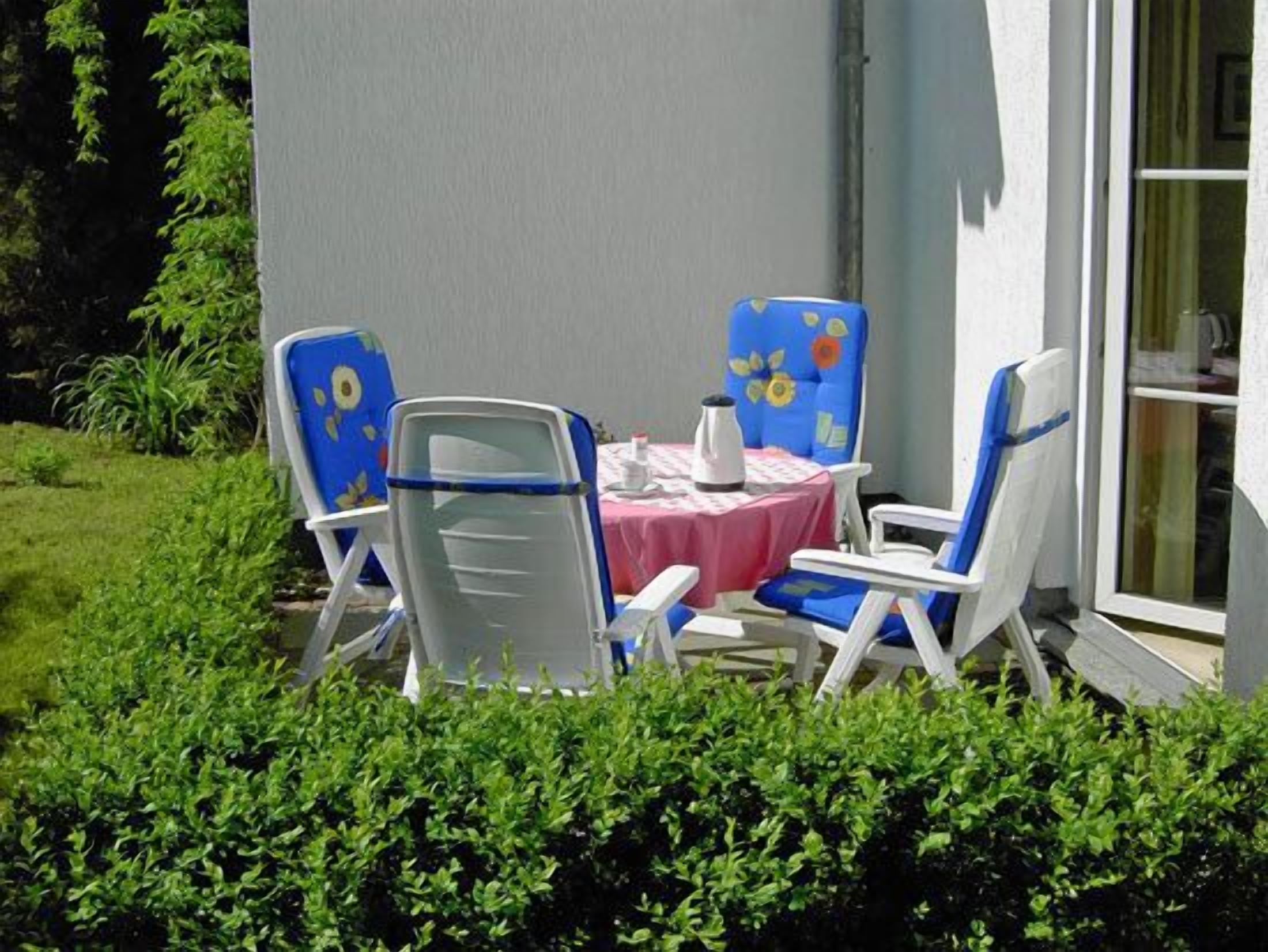 An outdoor seating area with a table and chairs, surrounded by greenery.