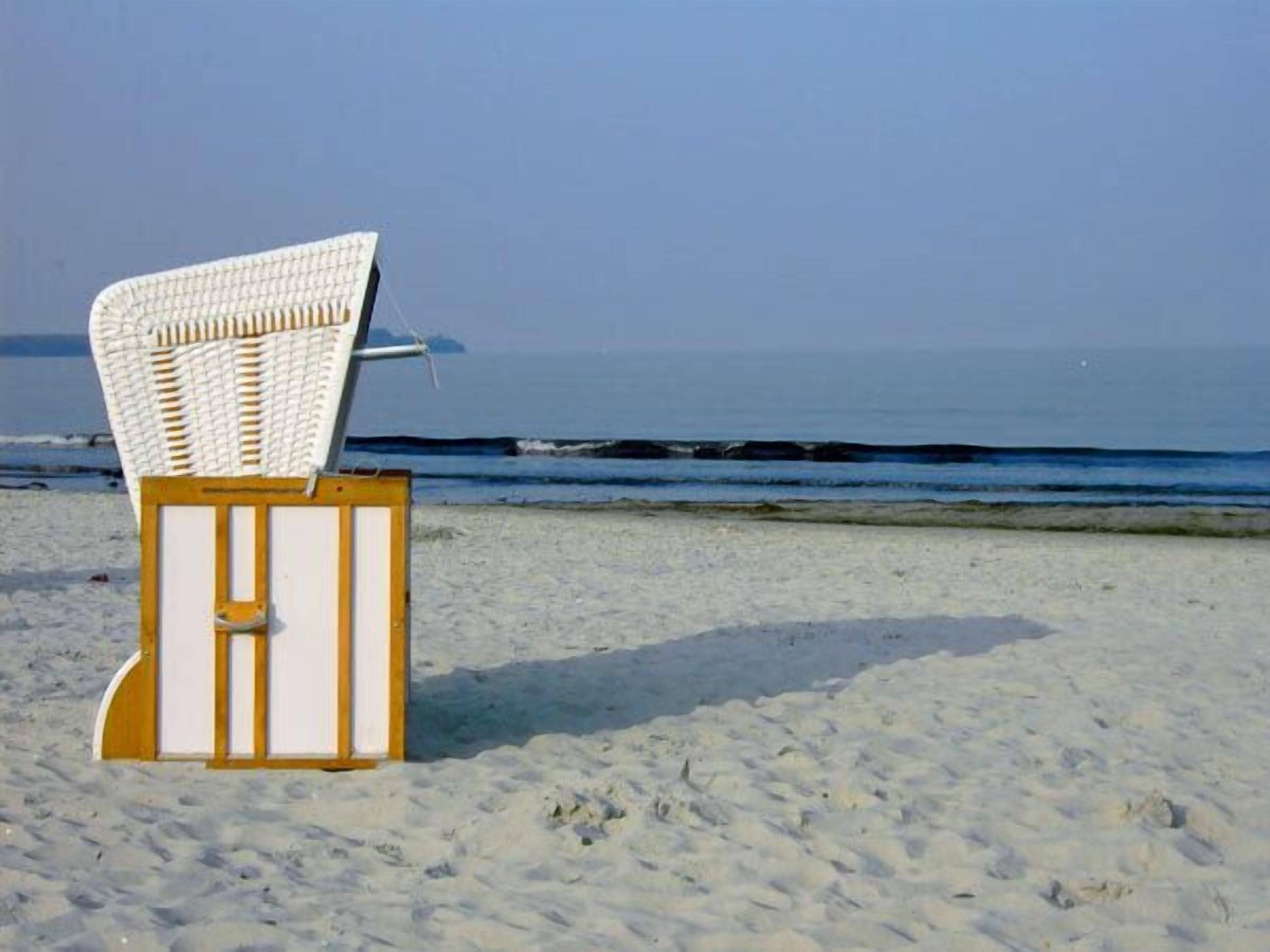 Ein Liegestuhl am sandigen Strand, im Hintergrund das Meer.