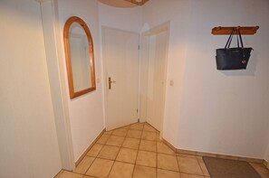 Een hal met een betegelde vloer, een spiegel met houten lijst, een deur en een hangende tas.