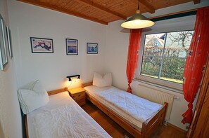 Een slaapkamer met twee bedden, een raam met gordijnen, en drie ingelijste foto’s aan de muur.