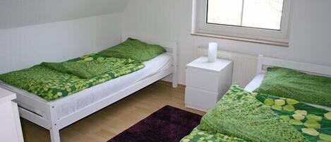 A room with two single beds, a window, a radiator, and a white nightstand.