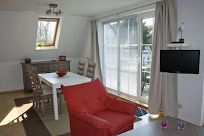 A room with a dining table, chairs, a red armchair, a television, and a window with blinds. - 1st floor, just 900 meters from the beach, with a washing machine, balcony, and internet/Wi-Fi (Breege)