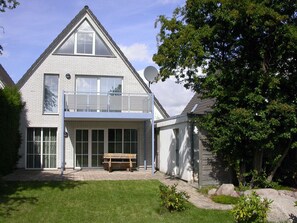 Ein zweistöckiges Haus mit Balkon, Satellitenschüssel und Bank im Vorgarten.