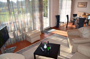 Ein Wohnzimmer mit einer Couch, einem Couchtisch mit Flasche und Fernbedienung sowie einem Fernseher.