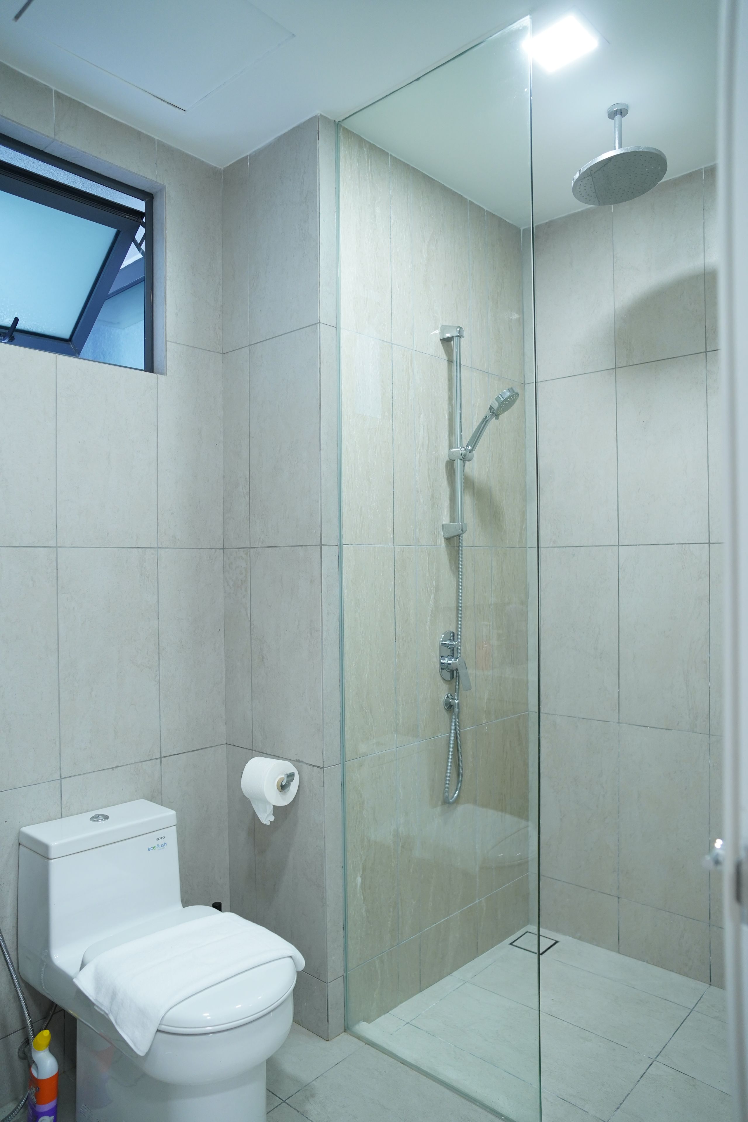 A modern bathroom with a glass-enclosed shower, a toilet, and a window.