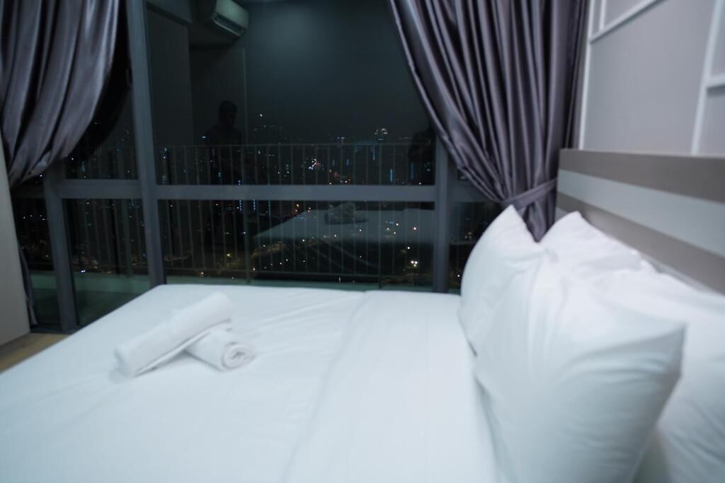 Habitación de hotel con una cama grande, vistas de la ciudad de noche y un balcón con barandilla.