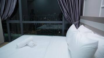 Habitación de hotel con una cama grande, vistas de la ciudad de noche y un balcón con barandilla.