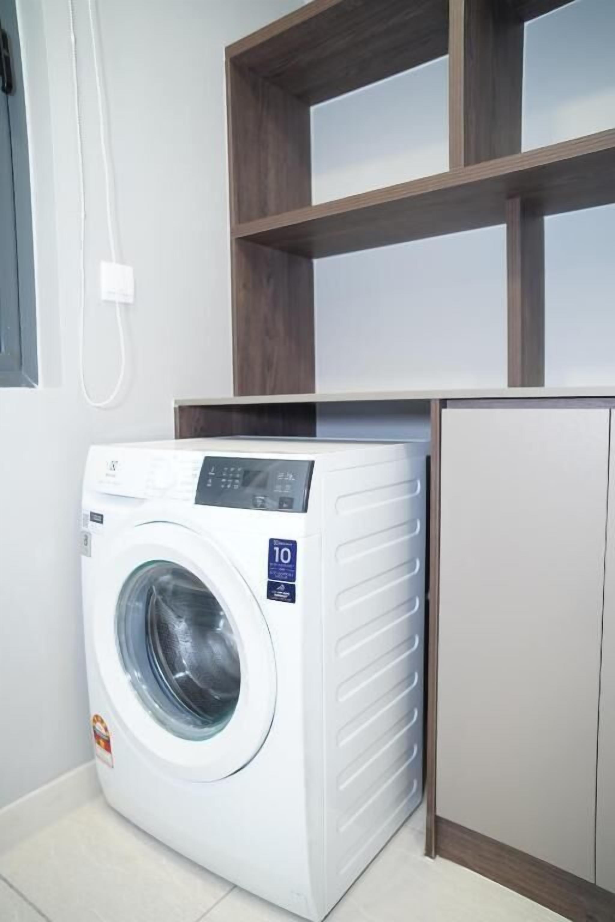 Un lavadero compacto y moderno con lavadora y secadora integradas, estantes de madera arriba y un refrigerador pequeño.