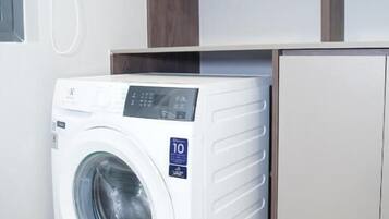 Un lavadero compacto y moderno con lavadora y secadora integradas, estantes de madera arriba y un refrigerador pequeño.