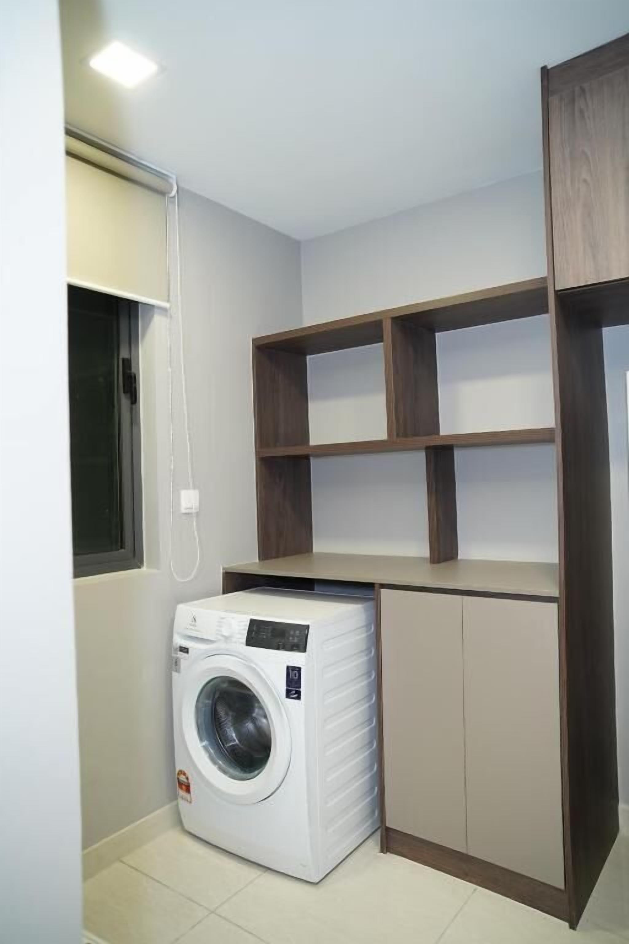 A laundry room with a washing machine, wooden shelves, and cabinets.