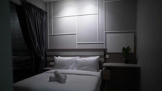A hotel room with a bed, a nightstand, a potted plant, and a wall-mounted panel.