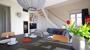 Una sala de estar moderna con una escalera, un comedor con una mesa dispuesta para dos personas y un jarrón con tulipanes.