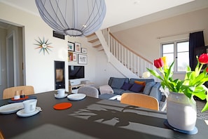 A modern living room with a staircase, a dining area with a table set for two, and a vase with tulips. - Close to the beach and with a lake view, spread over 2 floors, with a washing machine, sauna, and internet (Dranske)
