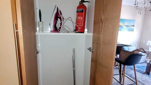 Een badkamer met een douche, toilet, een bezem, een bus met stofspray en een handdoekhouder.