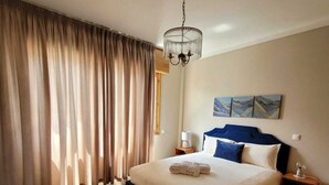 Een hotelkamer met een groot bed, een kroonluchter, een raam met gordijnen en kunst aan de muur.