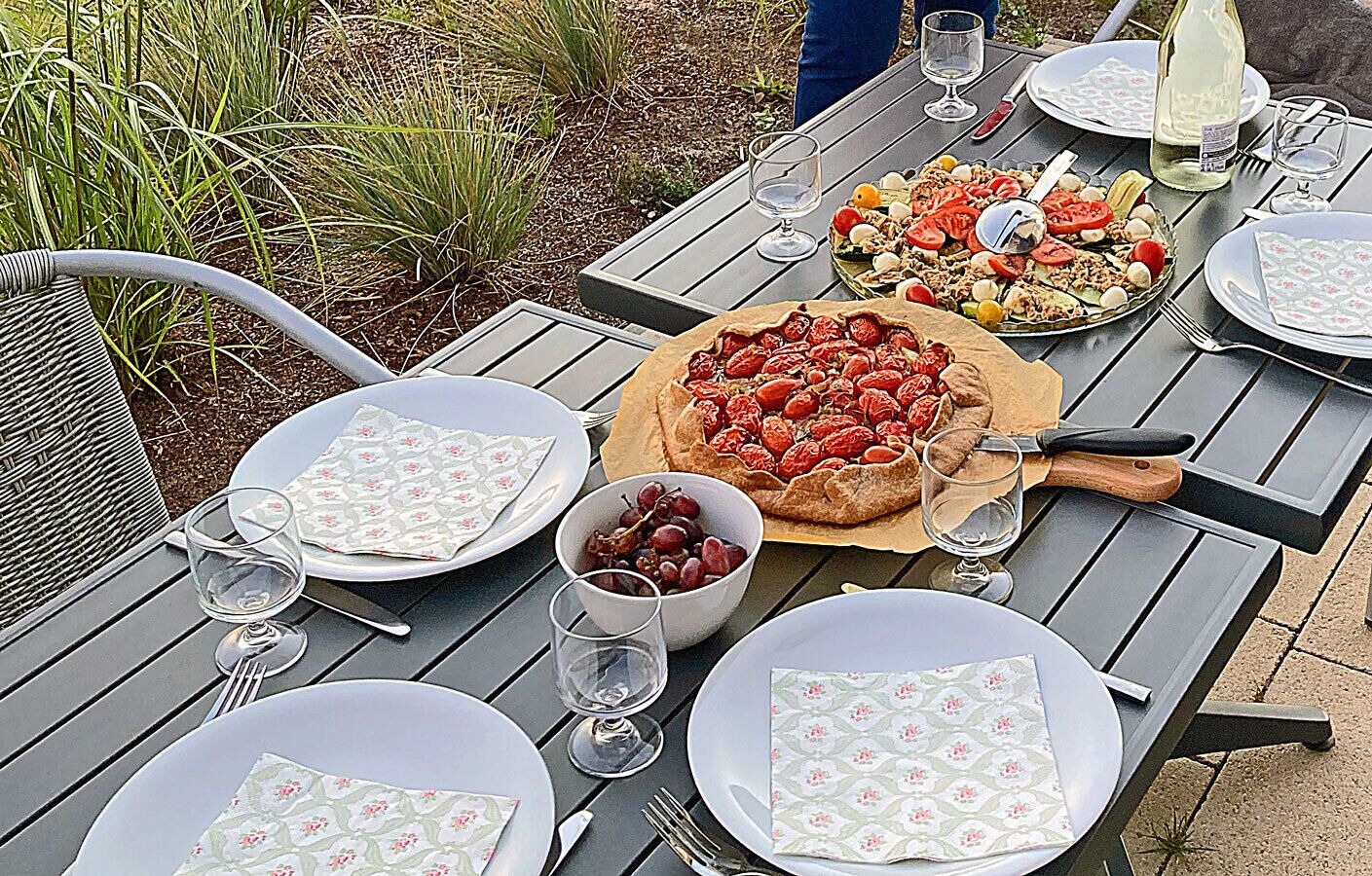 An outdoor dining table with plates, glasses, and a pizza.