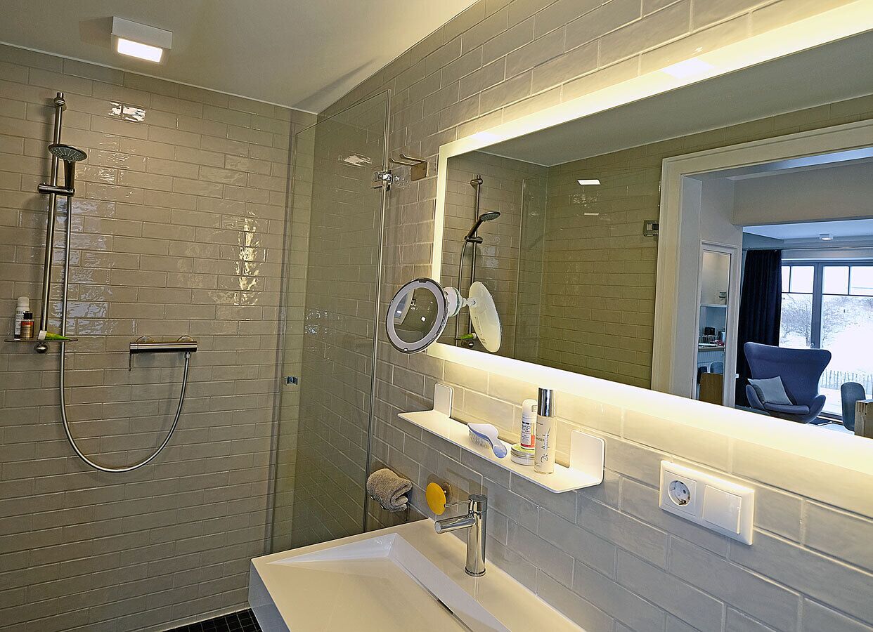 Ein modernes Badezimmer mit einer gläsernen Duschkabine, einem Waschbecken mit Spiegel und einem Waschtisch mit Pflegeprodukten.