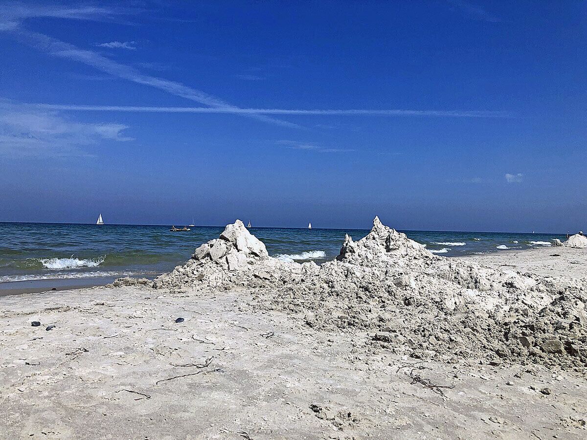 A rocky beach with clear skies and distant sailboats.