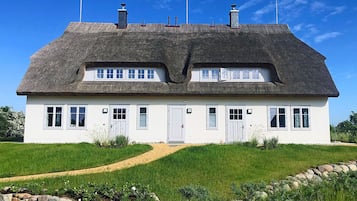 Una casa bianca con tetto di paglia, due camini e un muro di pietra in primo piano.