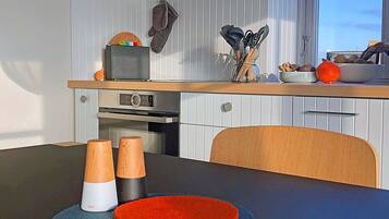 Una cucina moderna con mobili bianchi, un forno a microonde e un piano cottura. C'è una sedia di legno e un tavolo con un sottobicchiere rosso e dosatori di sale.