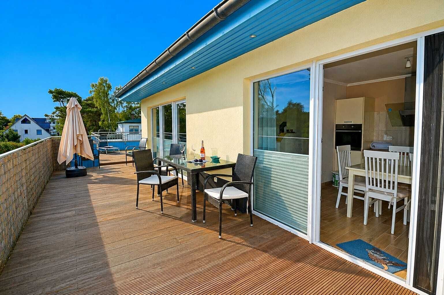 Ein Balkon mit Tisch und Stühlen, eine Schiebetür zu einer Küche und ein Blick auf einen Swimmingpool im Hintergrund.
