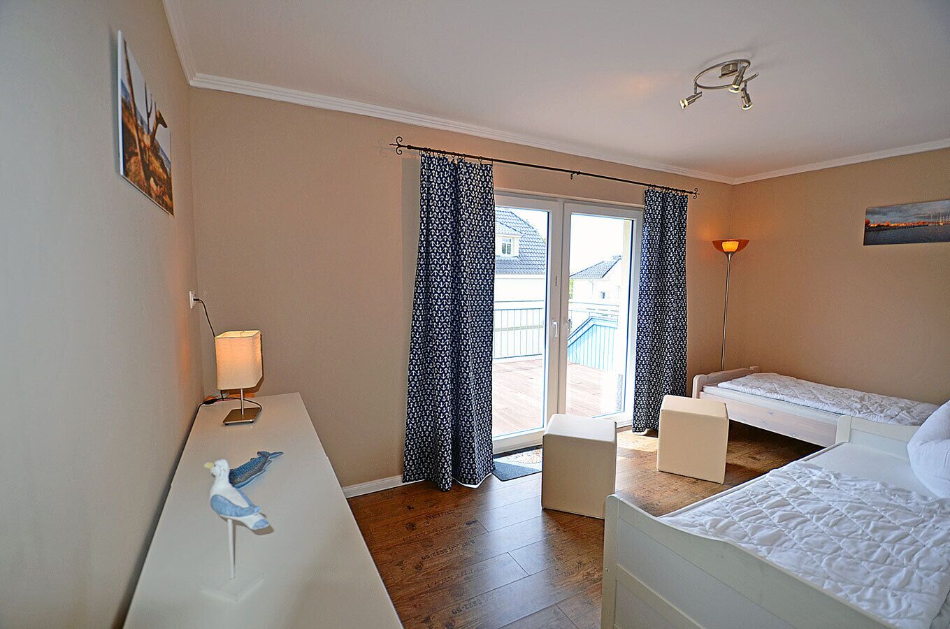 Ein Schlafzimmer mit Schreibtisch, zwei Betten, einer Lampe und Blick ins Freie.