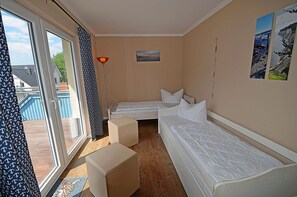 Ein Zimmer mit zwei Betten, einem Fenster, einem Gemälde und einer Lampe.