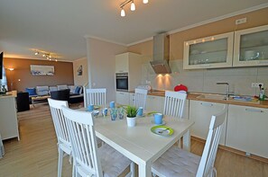 Eine moderne Küche mit weißen Schränken, einem Esstisch mit Stühlen und einem Wohnbereich mit Sofa und Couchtisch.