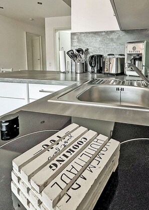 A kitchen with a stainless steel sink, a coffee maker, and a stack of white blocks with Hebrew text. - Vacation rental with a view of the water, sleeps up to 5 people with 2 bedrooms, just 60 meters from the water (Dranske)