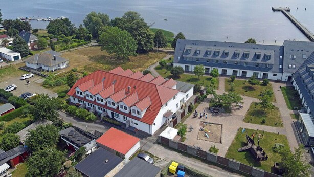 A residential area with houses, a large building with a red roof, and a dock extending into a body of water. - Vacation rental with a view of the water, sleeps up to 5 people with 2 bedrooms, just 60 meters from the water (Dranske)