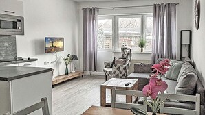 A modern kitchen with a microwave, dining table, and chairs. There is a living area with a sofa, a coffee table, and a TV. A window with curtains is visible. - Vacation rental with a view of the water, sleeps up to 5 people with 2 bedrooms, just 60 meters from the water (Dranske)