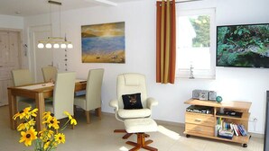 Ein Wohnzimmer mit Essbereich, Fernseher und Bücherregal.