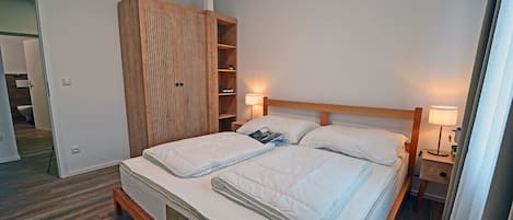 A bedroom with a bed, bedside lamps, a wardrobe, and a nightstand.