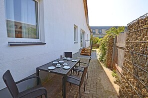 An outdoor patio with a table set for dining, a chair, and a white wall with windows. - Apartment complex in a quiet location, just 80 meters from the water, 2 bedrooms (Dranske)