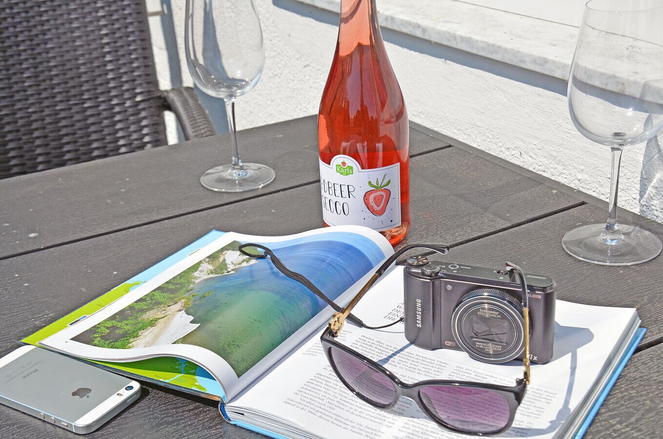 Een tafel met een boek, een camera, een smartphone, een biertje en twee glazen wijn.