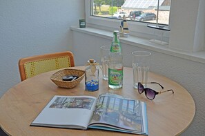 Une table ronde avec un magazine, un flacon de lotion après-rasage Merkur, un verre, une paire de lunettes de soleil et un objet décoratif.
