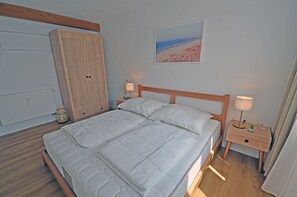 Een slaapkamer met een bed, nachtkastjes, een kledingkast en een schilderij aan de muur.