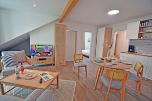 Een moderne woonkamer met televisie, bank en eethoek.