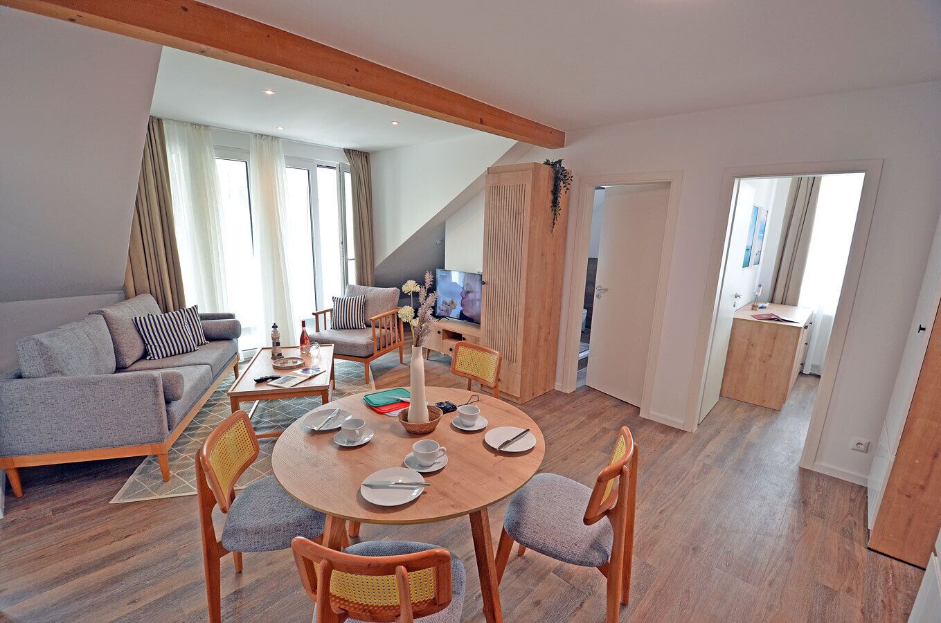En moderne stue med en sofa, et spisebord dækket til fire personer og et fjernsyn.