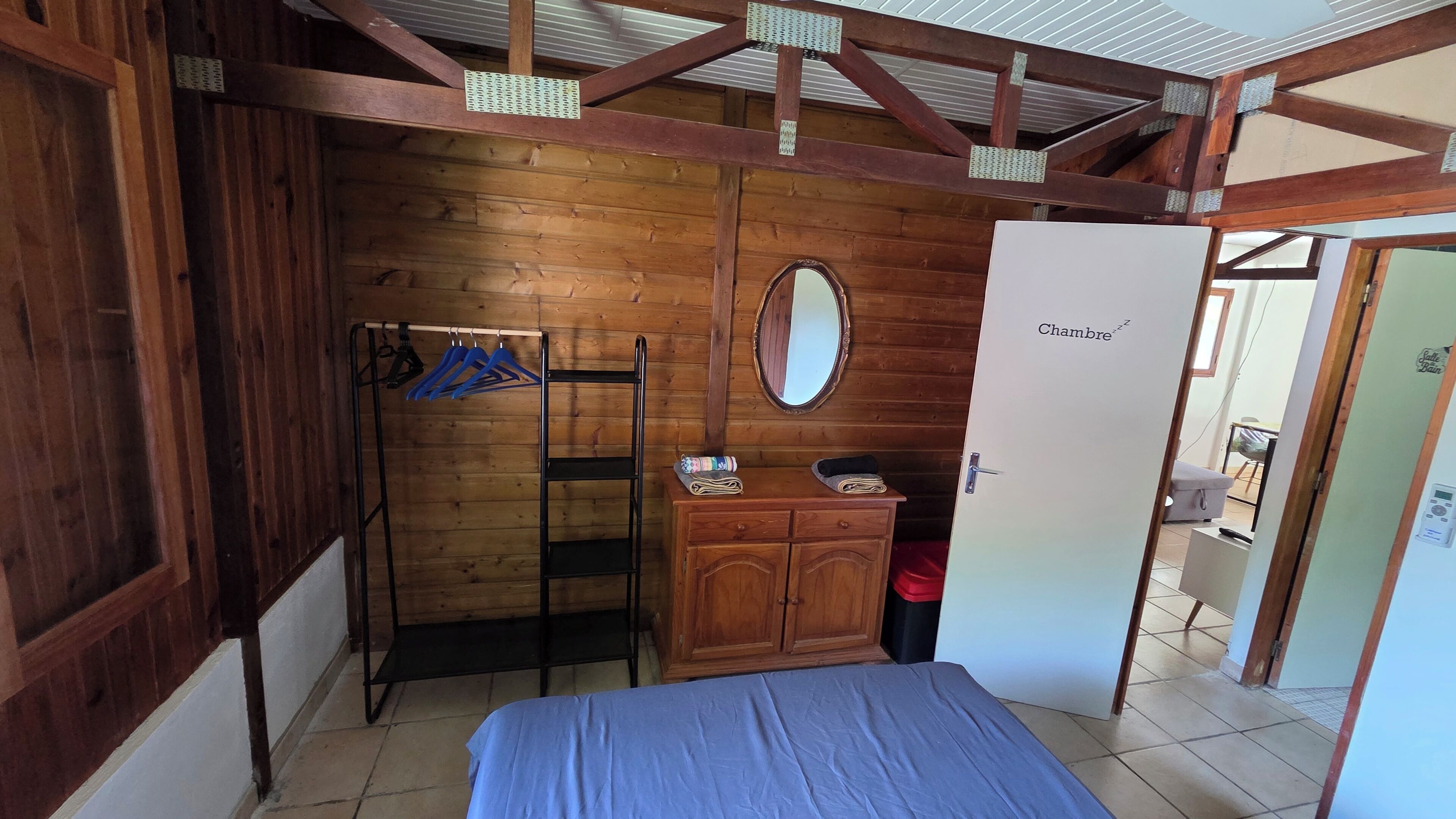 Ein Zimmer mit einem Bett, einem Holzschrank, einem Spiegel und einer Tür mit der Aufschrift 'Chambre'.