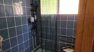 Ein Badezimmer mit Duschkabine aus Glas, gefliestem Boden, einem Fenster mit Vorhang und einem Mülleimer.